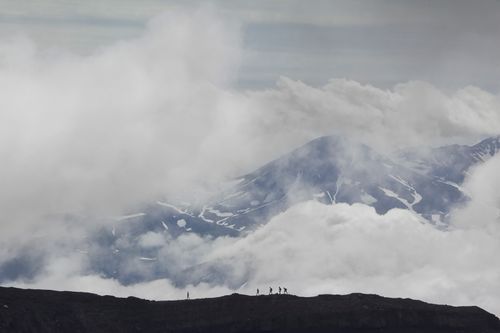 Free Hikers traverse a foggy mountain ridge in Kamchatka, surrounded by dramatic volcanic scenery. Stock Photo