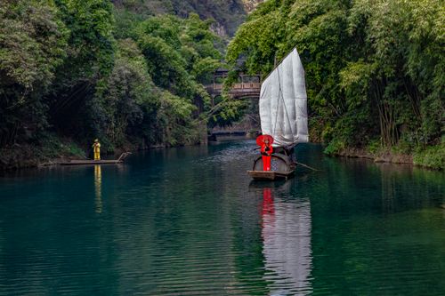 Free Wooden boats sail a tranquil river surrounded by lush greenery and traditional architecture. Stock Photo