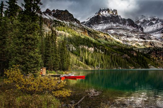 A tranquil mountain scene with a lake, red canoe, and forest under cloudy skies.