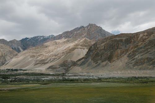 Picturesque scenery of empty grassy meadow located near rocky mountain ridge against cloudy sky in Hunza Valley