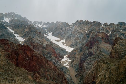 阴天映衬着雪坡，壮观的巨大粗糙岩石山脉构成了一幅景观