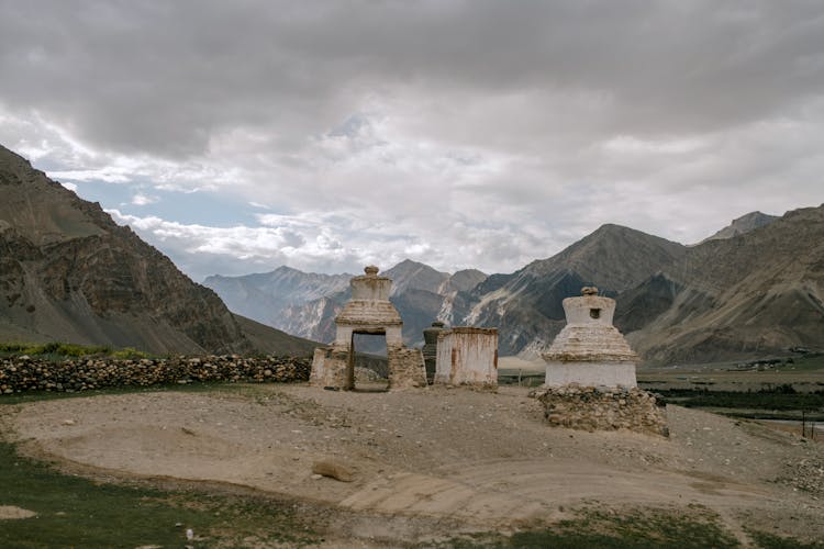 Old Buddhist Chorten Surrounded By Rocky Mountains Against Cloudy Sky