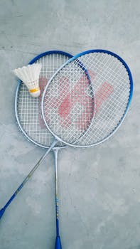 Top view of two badminton rackets and a shuttlecock on a concrete floor, perfect for sports-themed content.