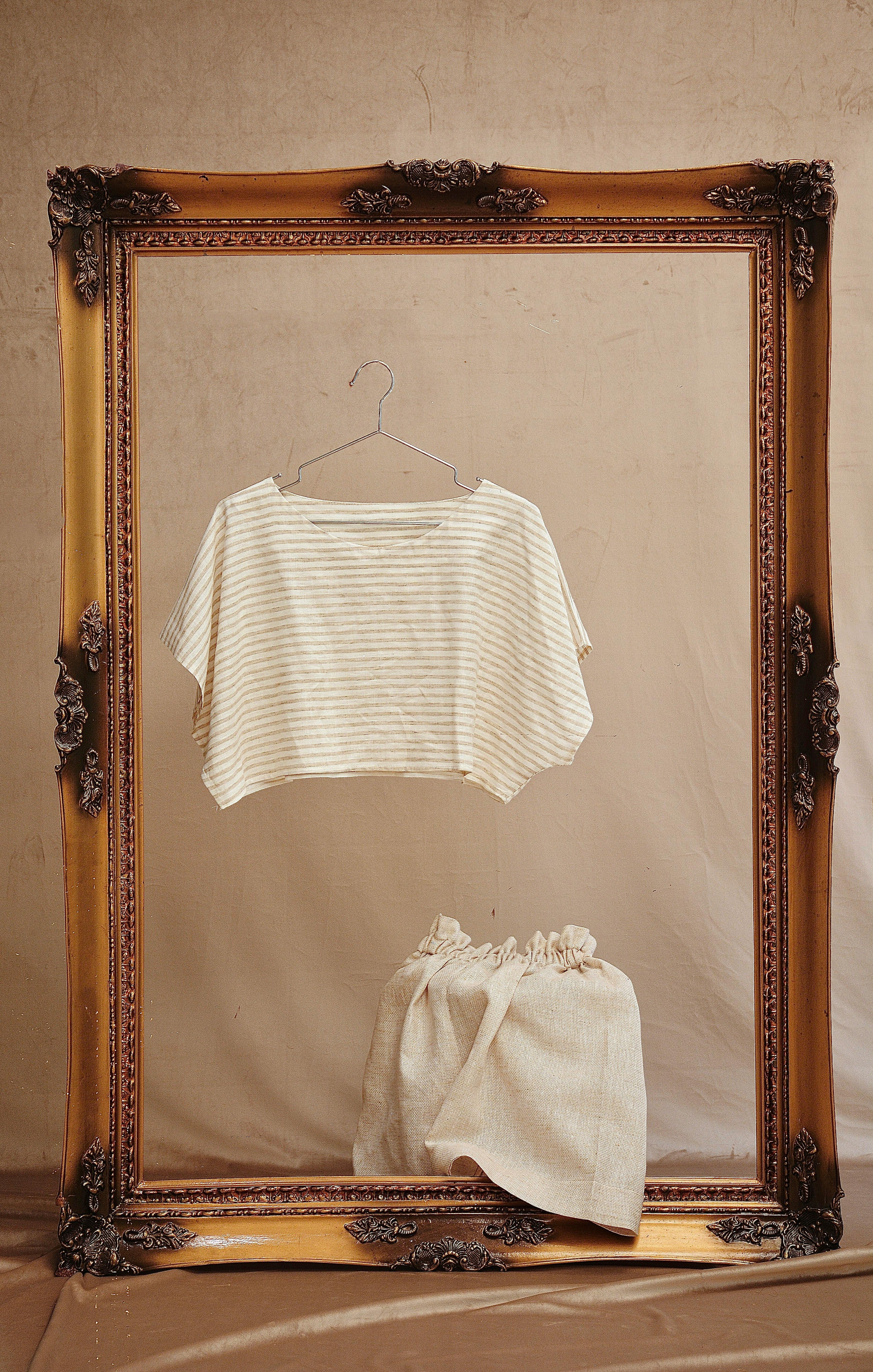 Contemporary feminine outfit on metal hanger between ornamental wooden frame on beige background