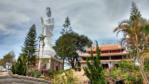 Free Large white Buddha statue and traditional temple surrounded by lush greenery in Vietnam. Stock Photo