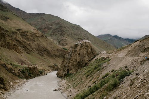 Picturesque scenery of wild river flowing among rough rocky mountains near old Buddhist Bardan Gompa monastery against foggy sky