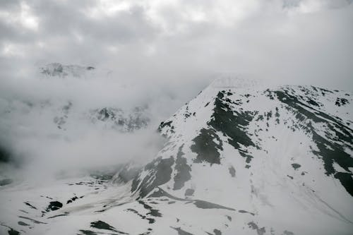 Breathtaking landscape of huge rocky mountain range covered with snow against cloudy sky in winter