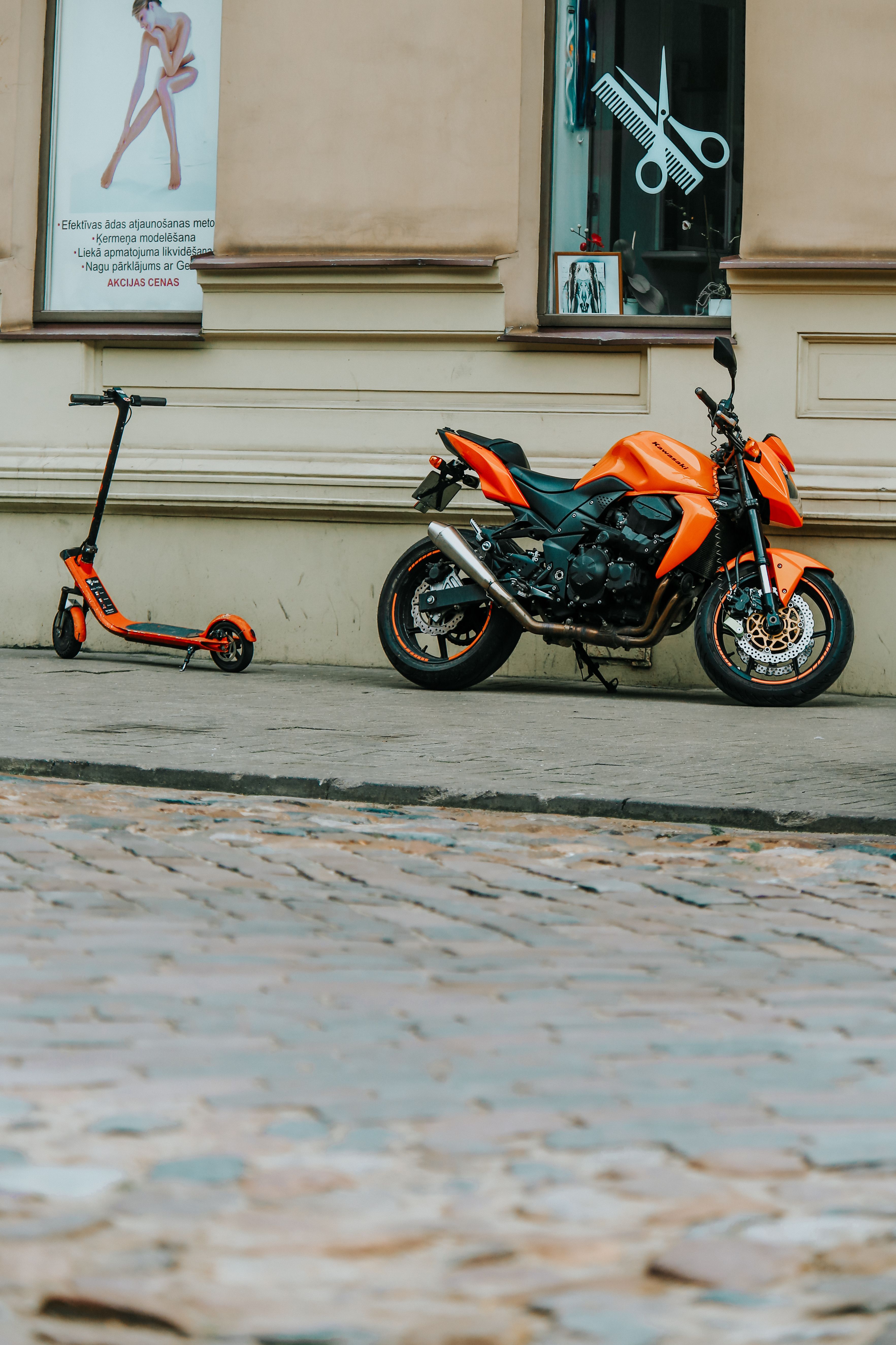 Vibrant orange motorbike and e-scooter parked on a cobblestone street in Riga, Latvia.