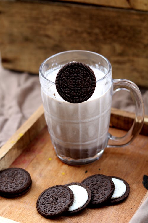Free From above of glass cup of cacao served with cookies consisting of two chocolate sugar black disk biscuits and sweet cream Stock Photo