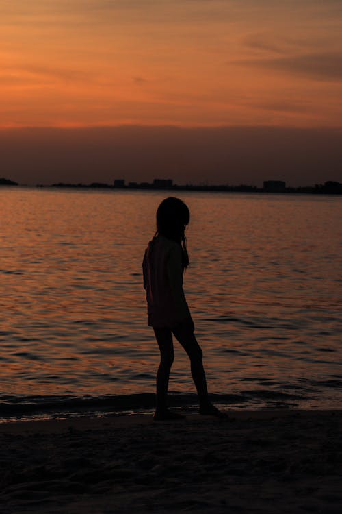 Silhouette of a Girl Standing on Beach during Sunset