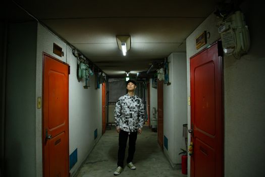 一位穿着时尚的亚洲男性站在公寓狭窄的带门走廊里