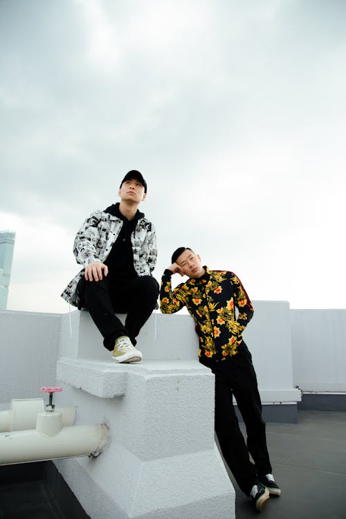 Full body of Asian males in trendy outfits on rooftop of building against cloudy sky