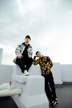 在大楼屋顶上，一位身着时尚服装的亚洲男性站在多云的天空下