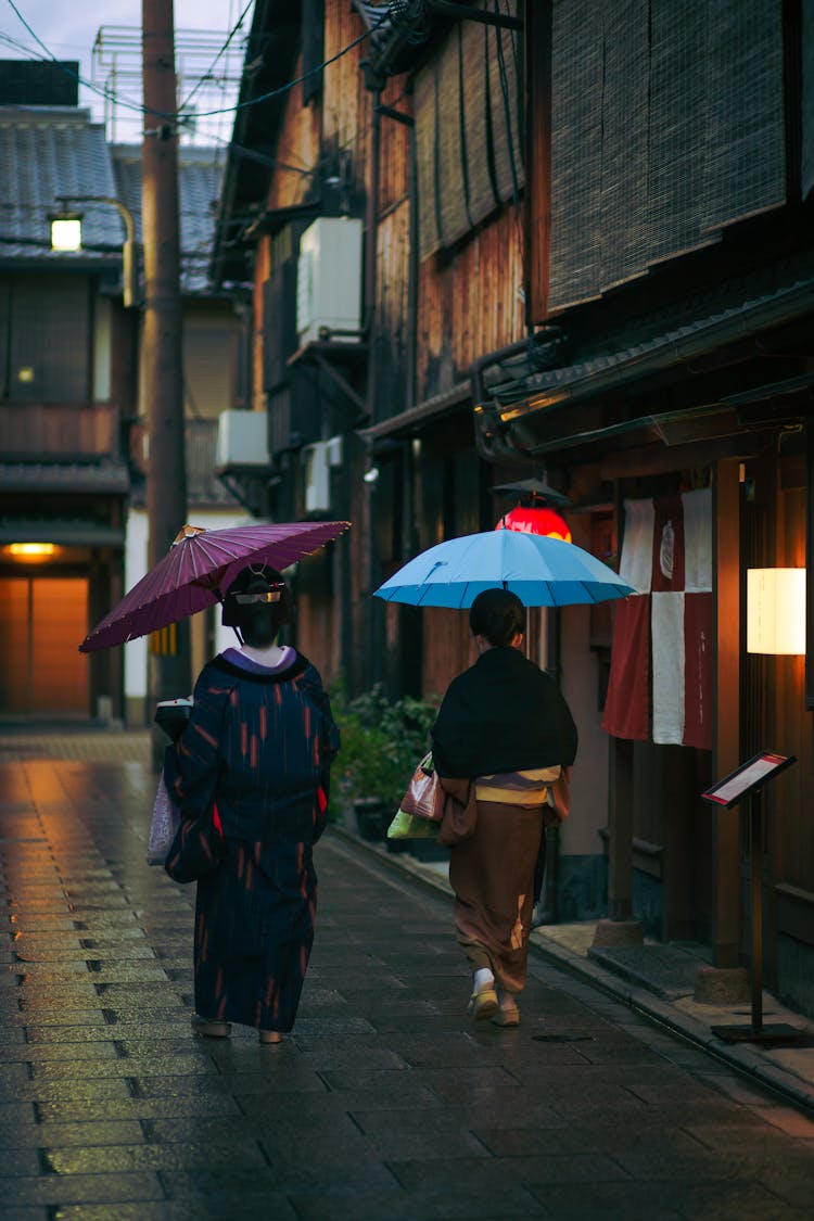 Woman In Traditional Outfits And Umbrellas Walking Together