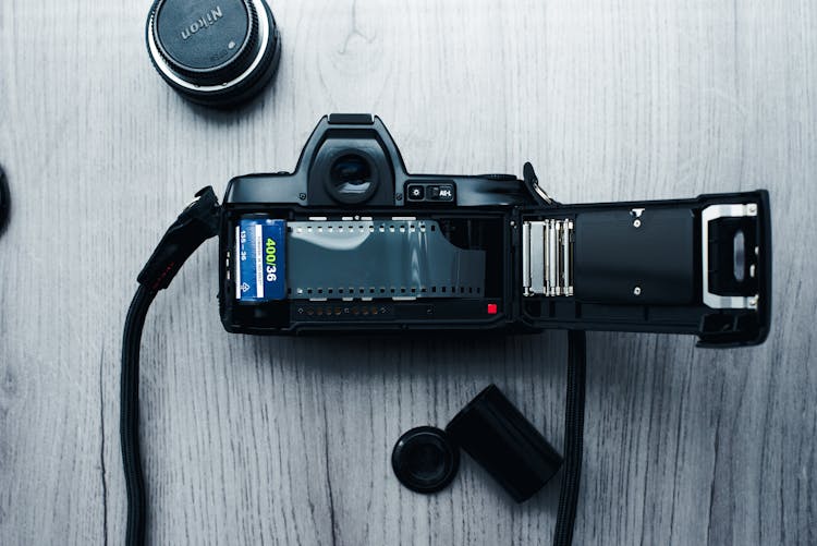 A Black Camera With Film Roll On Wooden Surface