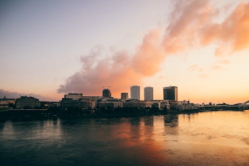 Amazing view of colorful sundown sky over calm river flowing near city with modern buildings