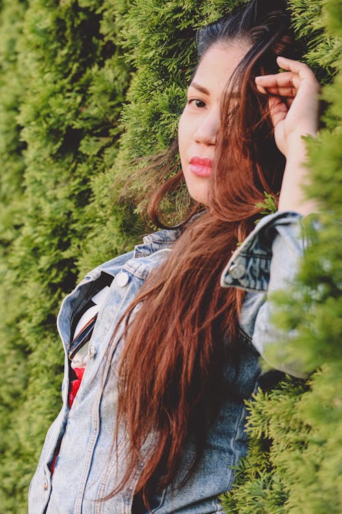 Woman in Denim Jacket Leaning on a Wall of Plants