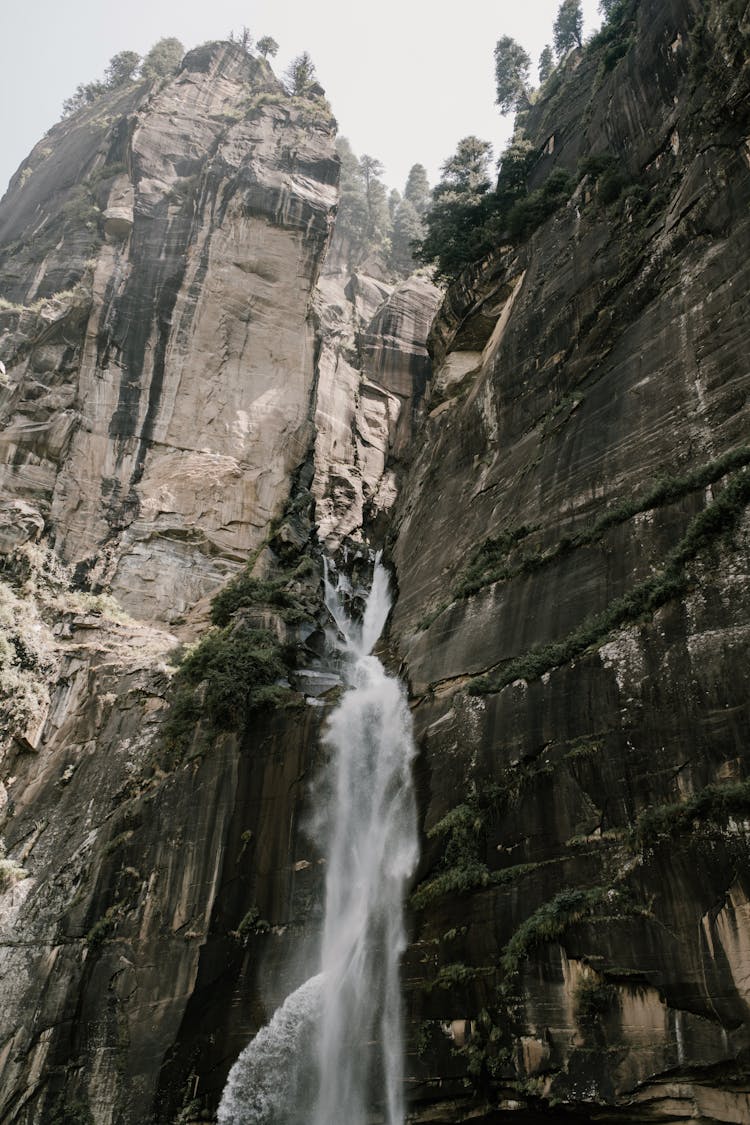 Rapid Waterfall Streaming Through Rocky Cliff In Wild Valley