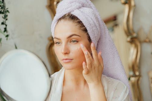 Free Woman With Head Towel Applying Face Cream Stock Photo