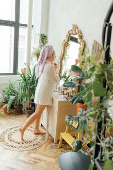Woman applying skincare product in a cozy, plant-filled bedroom.