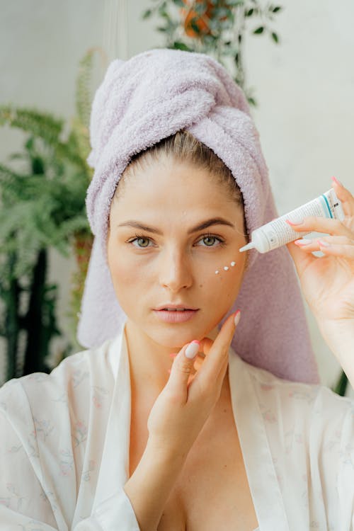 Free Woman in White Robe with Head Towel Holding a Facial Cream in Tube Stock Photo