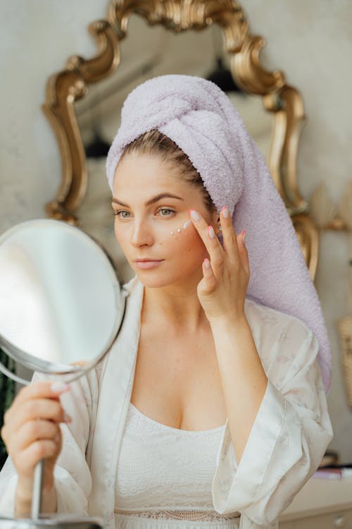 Free Woman Looking in the Mirror and Applying a Face Cream Stock Photo