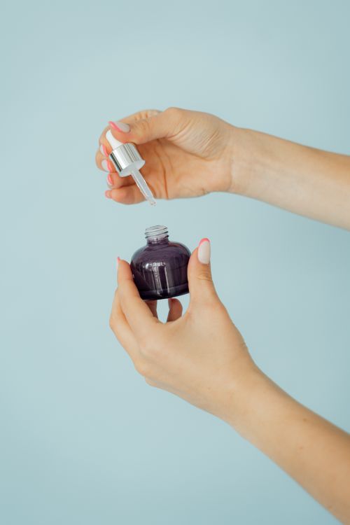 Free Close-up of a woman holding a cosmetic dropper bottle against a light blue background. Stock Photo