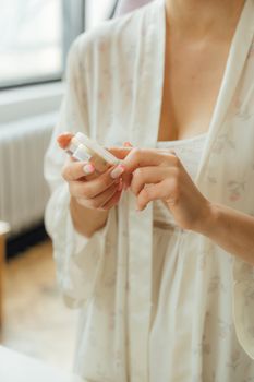 Close-up of a woman in a white floral robe holding a lip balm. Ideal for beauty or skincare themes.