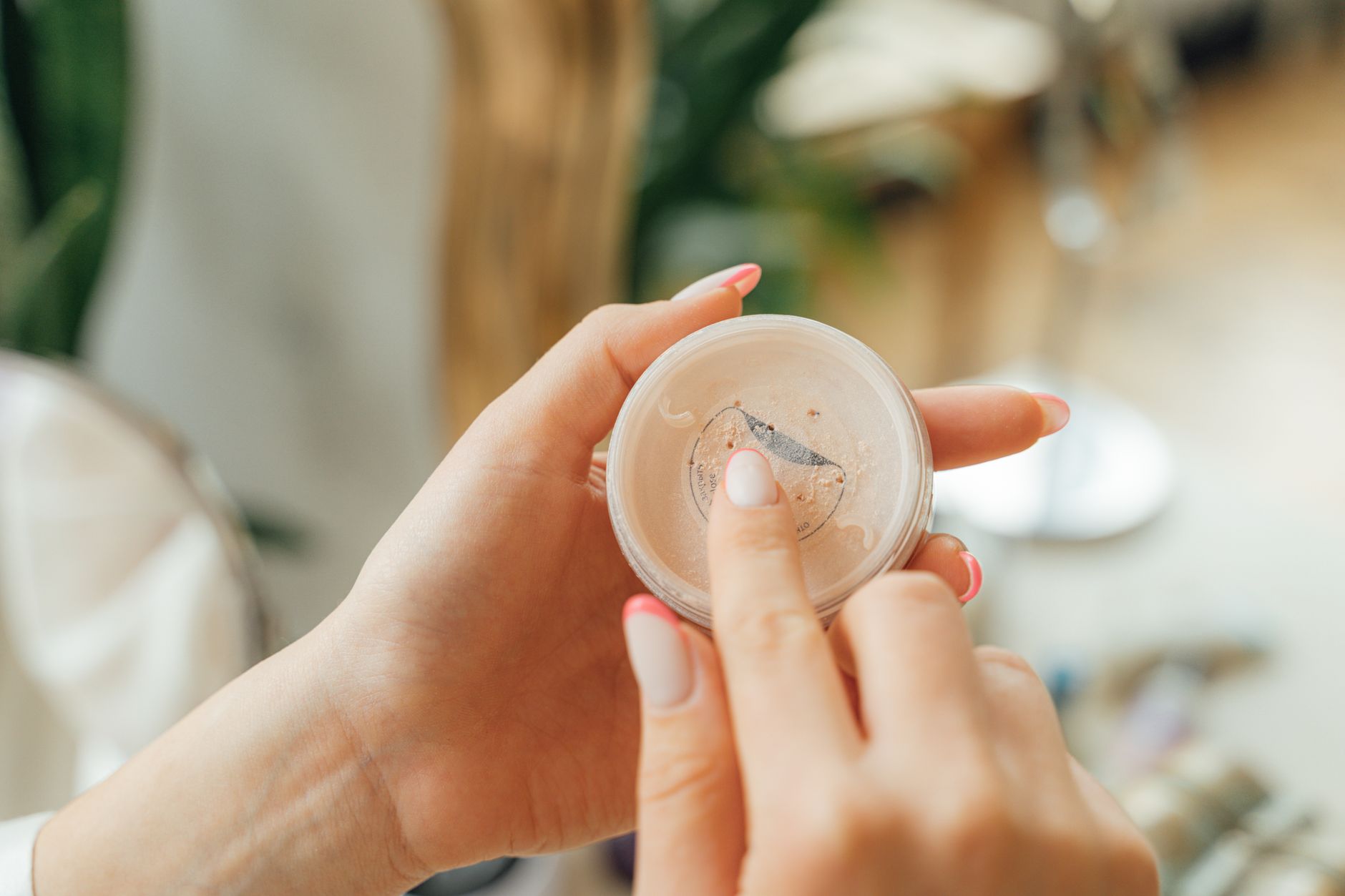 Woman's hands applying face powder from a plastic container, showing manicured nails.