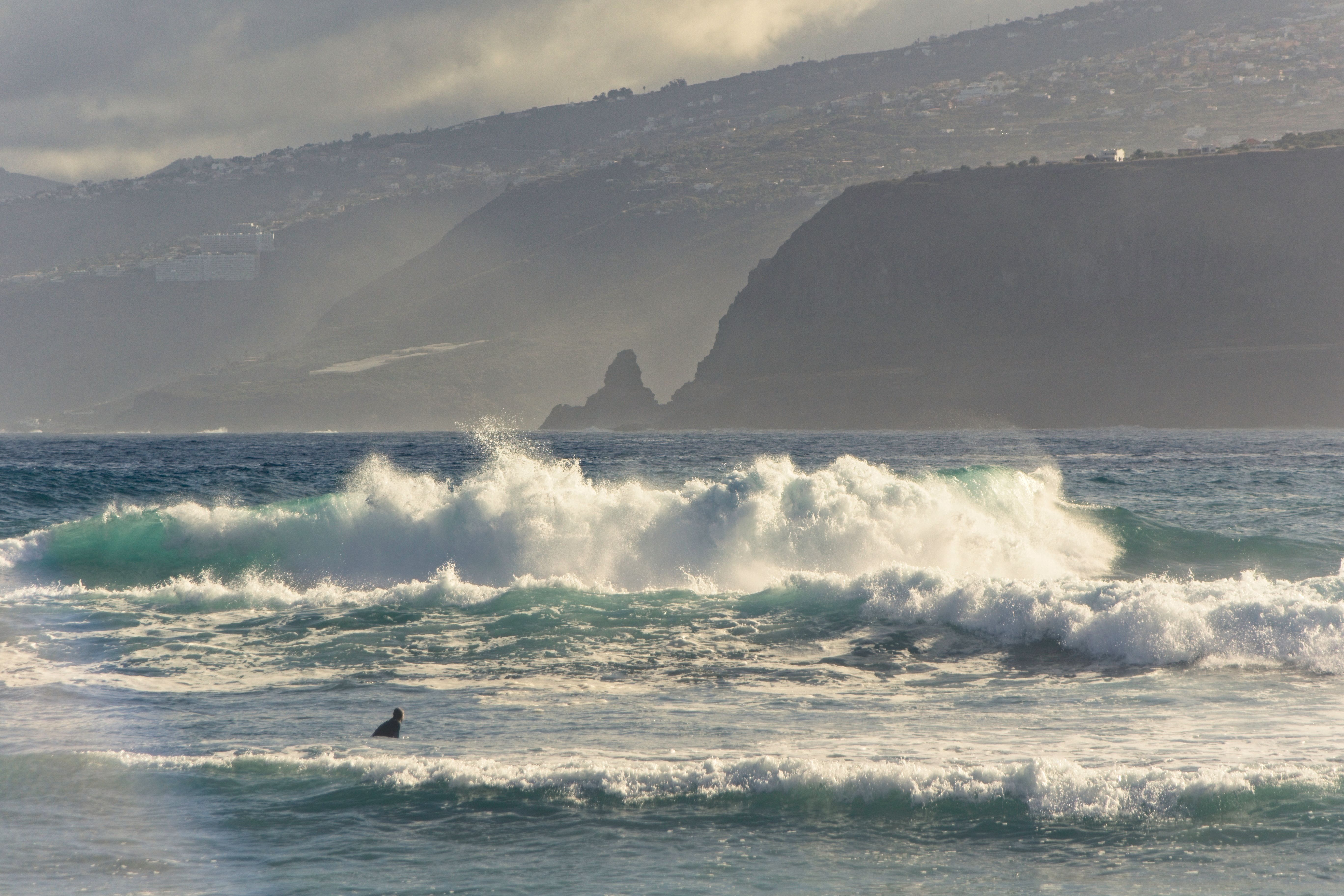 Dynamic waves crash against a rugged coastal mountain backdrop, capturing nature's raw power.