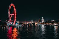 Scenery of contemporary city waterfront with tall observation wheel and modern towers illuminated by bright multicolored lights at night