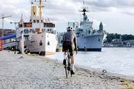 Man in Black T-shirt Riding Bicycle on Gray Concrete Pavement Near White and Blue Ship