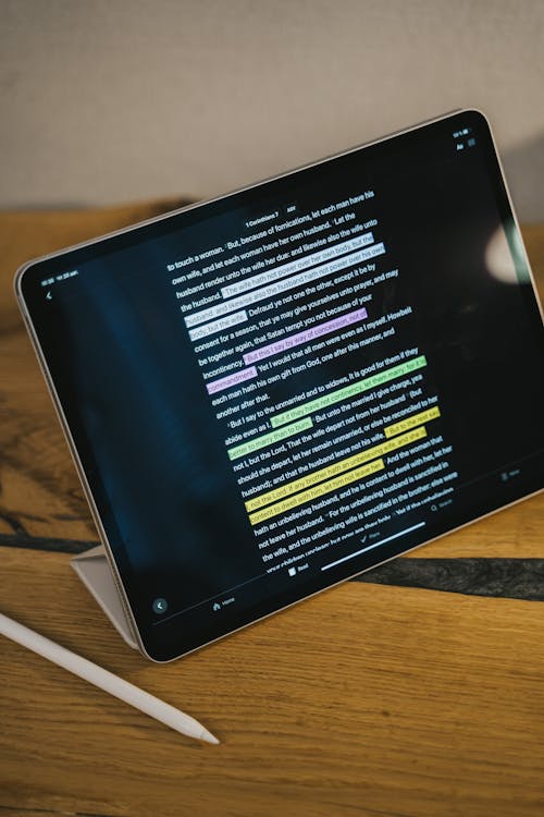 Close-Up Shot of a Tablet beside a Stylus on a Wooden Surface