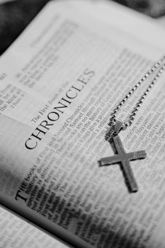 Black and white photo of a Bible page with a cross pendant on top, symbolizing faith.
