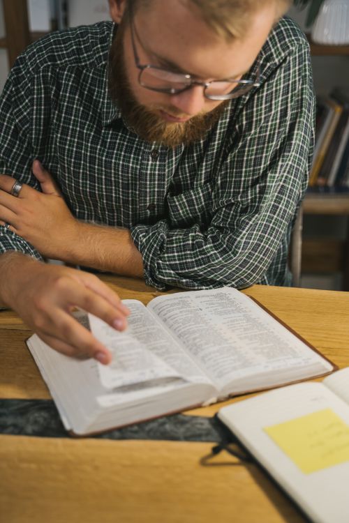 Free Bearded man engrossed in reading an open Bible indoors at a wooden table. Study and faith concept. Stock Photo