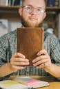 Close-Up Shot of a Bearded Man with Eyeglasses Holding a Holy Bible while Looking at Camera