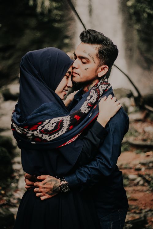 Free A loving couple embracing outdoors by a waterfall, showcasing affection and cultural attire. Stock Photo