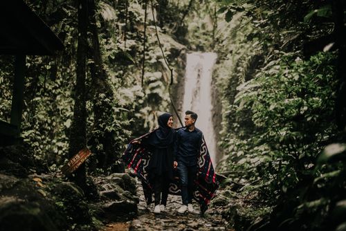 Free Happy couple walking hand in hand near waterfall in lush forest. Stock Photo