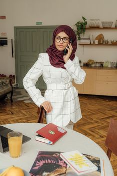 一位戴着头巾、身穿格子夹克的穆斯林妇女正在家里用智能手机通话