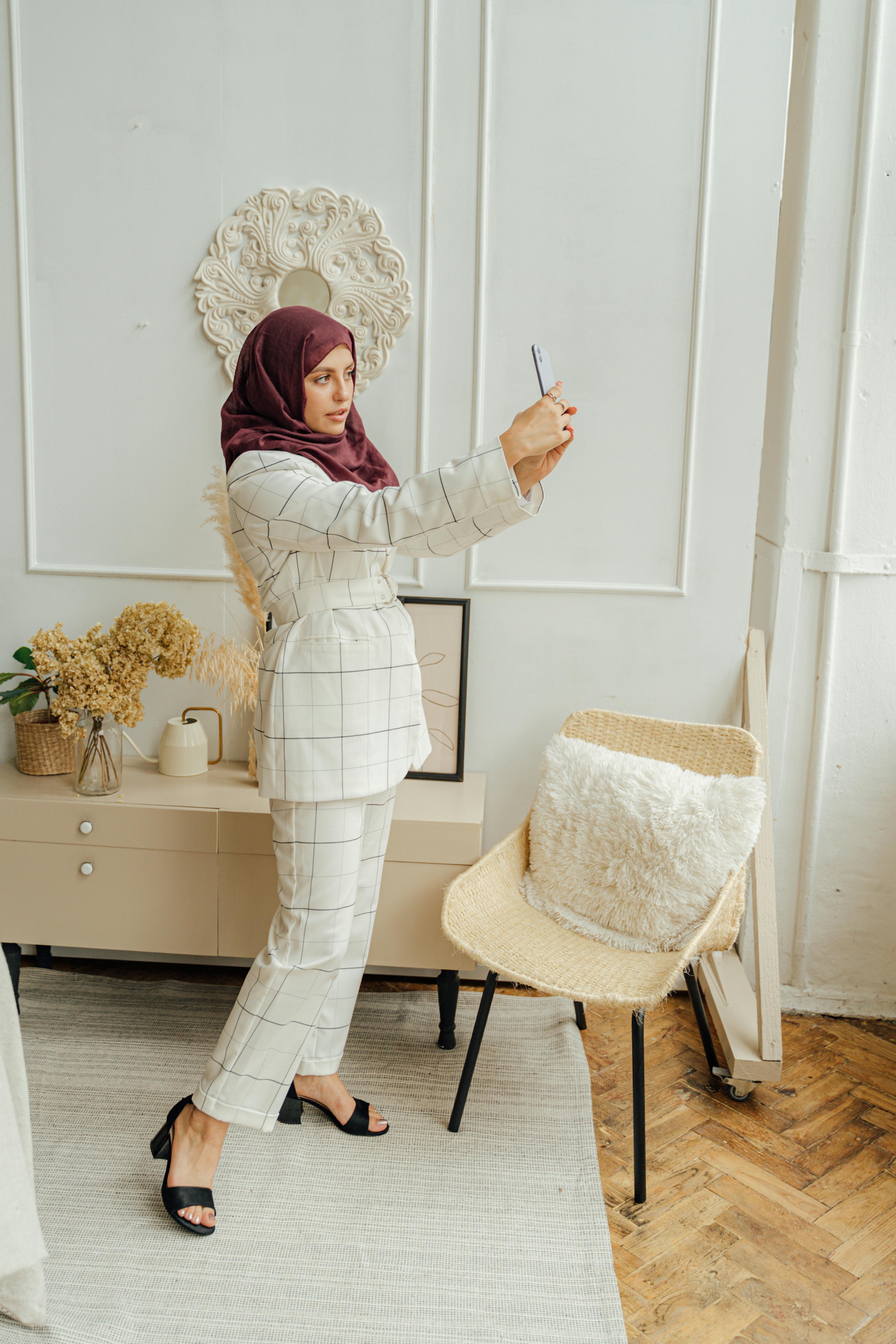 Elegant woman in formal attire taking a selfie indoors, showcasing modern technology and style.