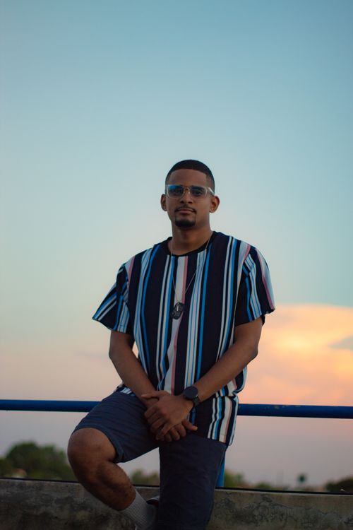 Free Stylish man in a striped shirt poses outdoors against a sunset sky, conveying a modern and fashionable vibe. Stock Photo