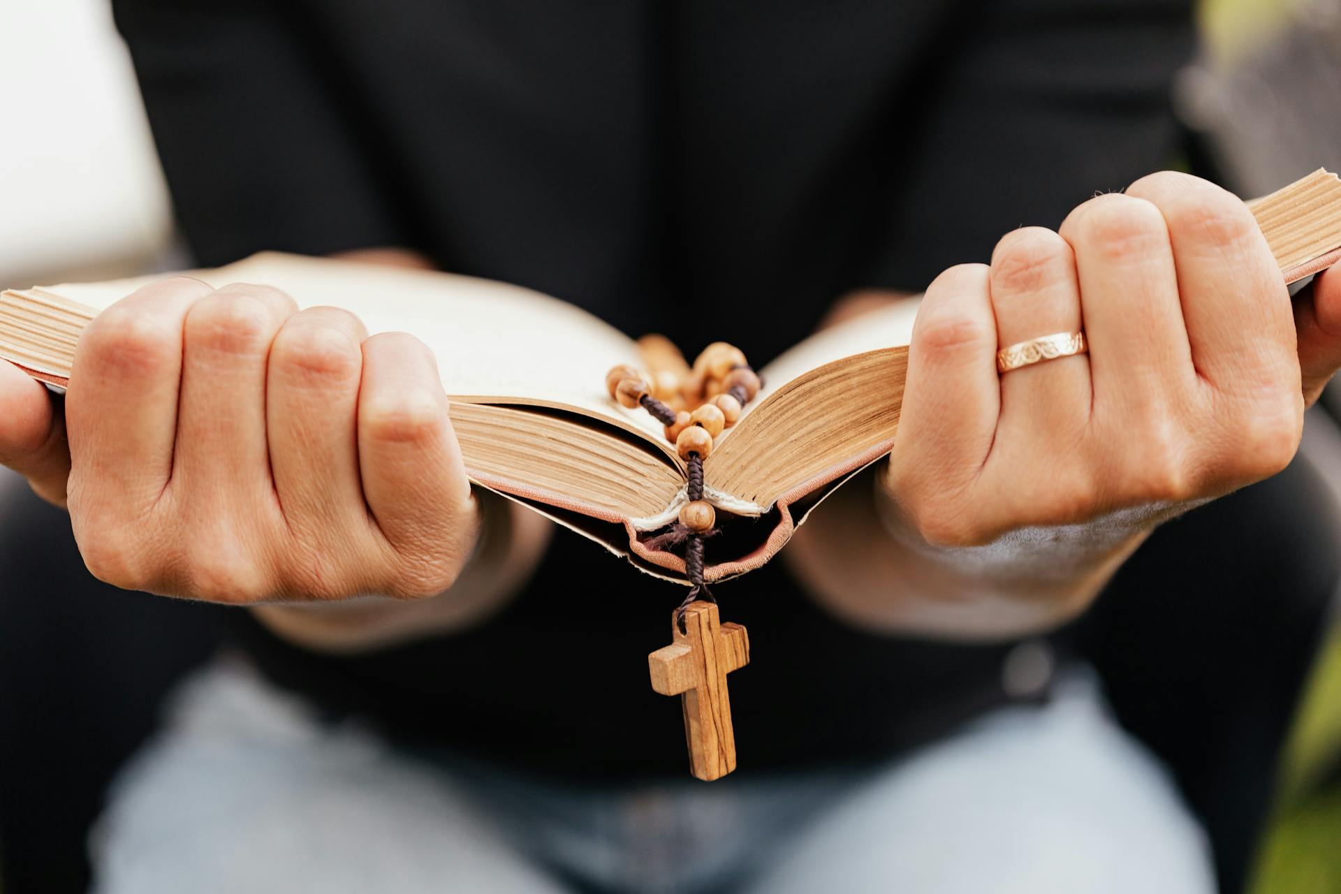 A close-up of hands holding an open Bible with a rosary, symbolizing faith.