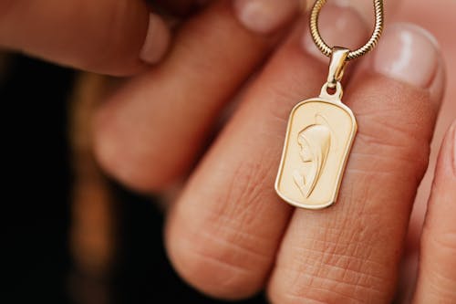 Close-Up Shot of a Person Holding a Gold Religious Pendant