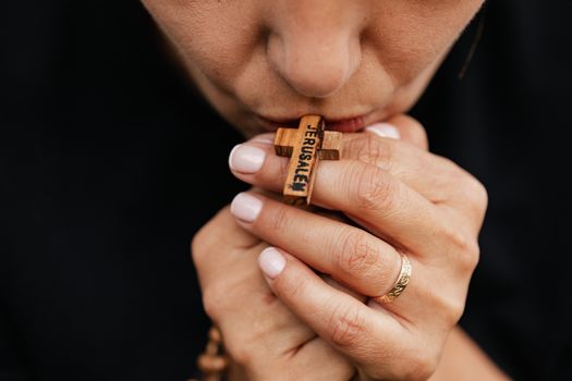 特写图像：一个人手持木制十字念珠，亲吻并祈祷