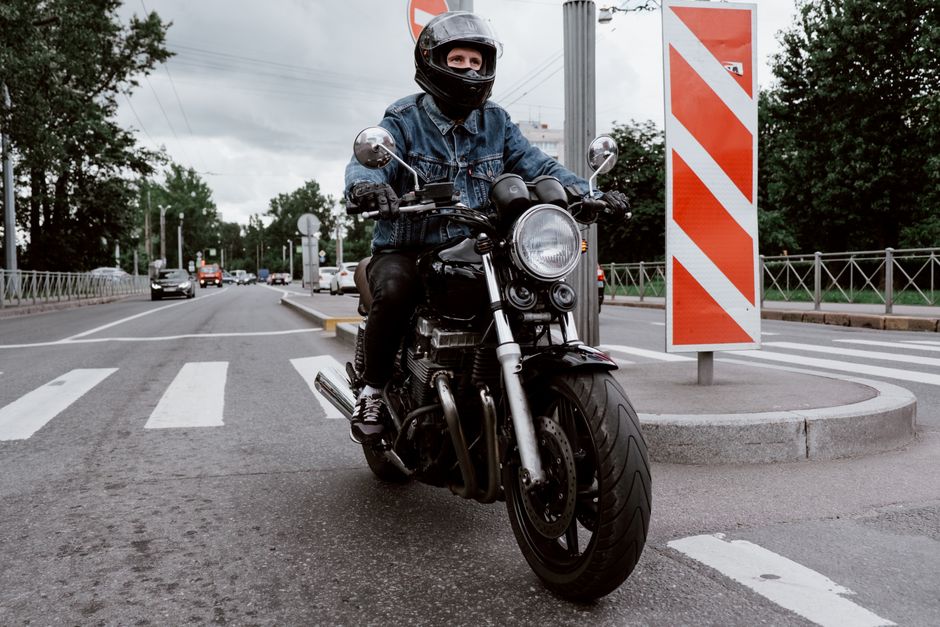 Motorcyclist in a denim jacket riding on an urban road with a crosswalk.