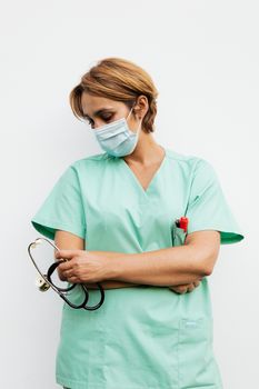 女医生戴着口罩，穿着绿色磨砂膏，拿着听诊器，摆出若有所思的姿势