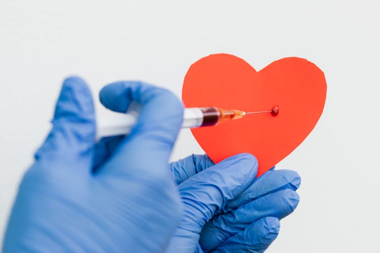 
A Person Wearing Latex Gloves Injecting A Heart Cutout