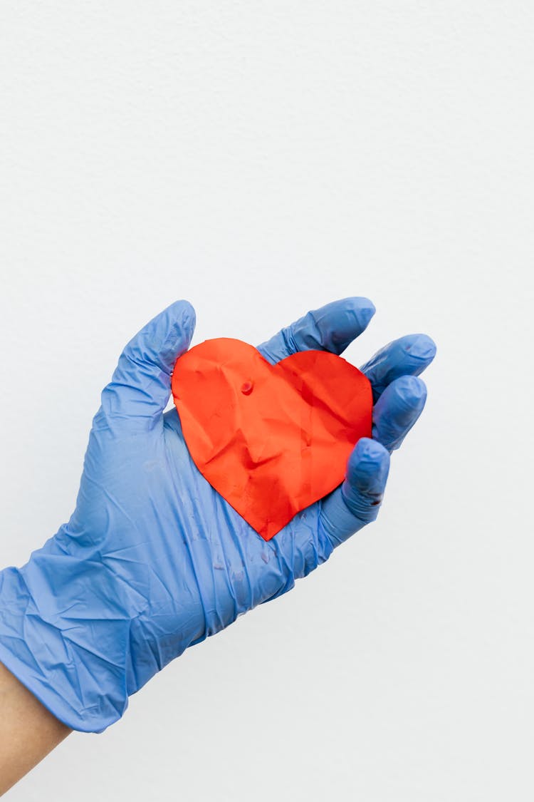 A Person Wearing Latex Gloves Holding A Heart Cutout