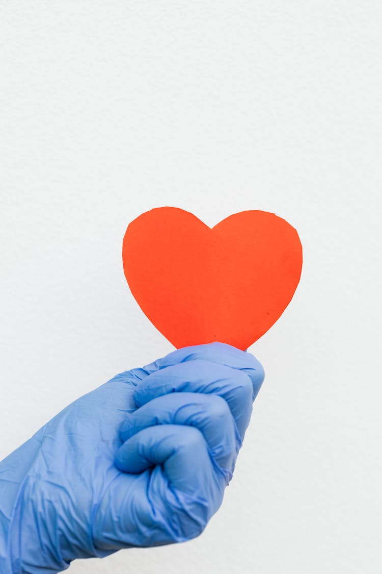 A Person Wearing Latex Gloves Holding A Heart Cutout