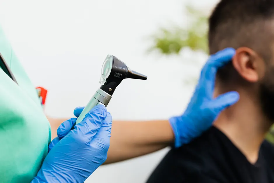 Professionnel de santé ganté tenant un otoscope face à l'oreille d'un patient lors d'un examen auditif